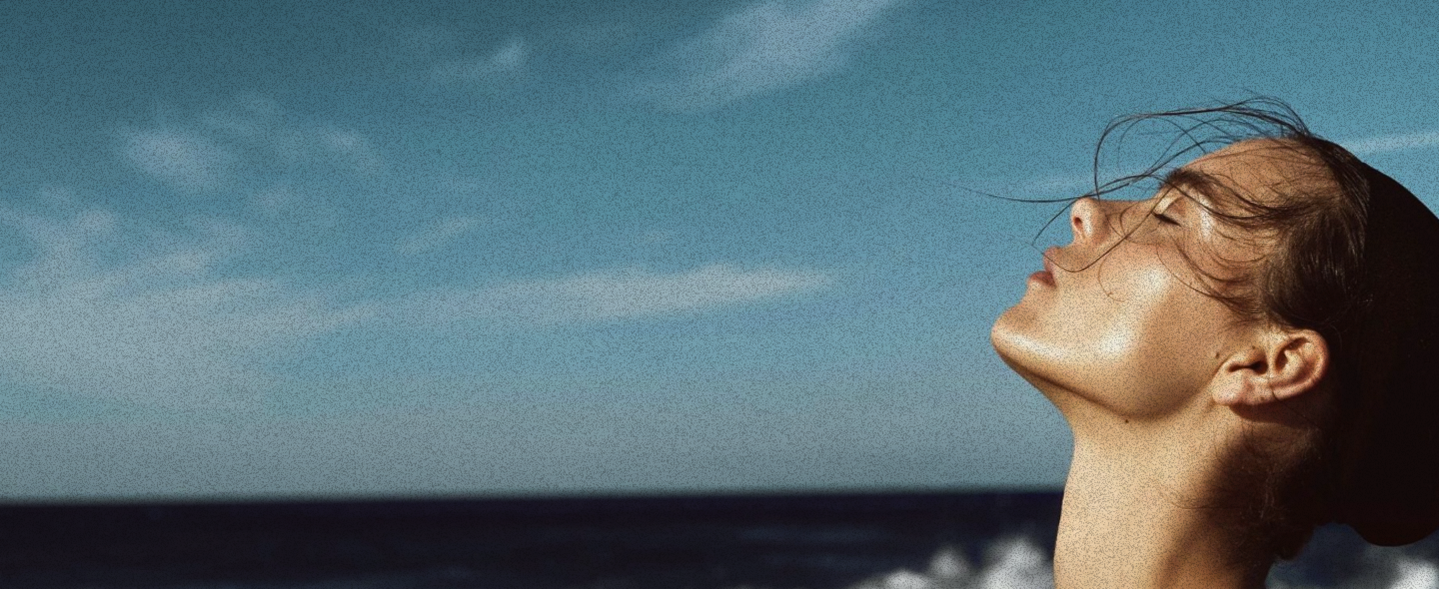 Person with eyes closed against a blue sky and ocean background